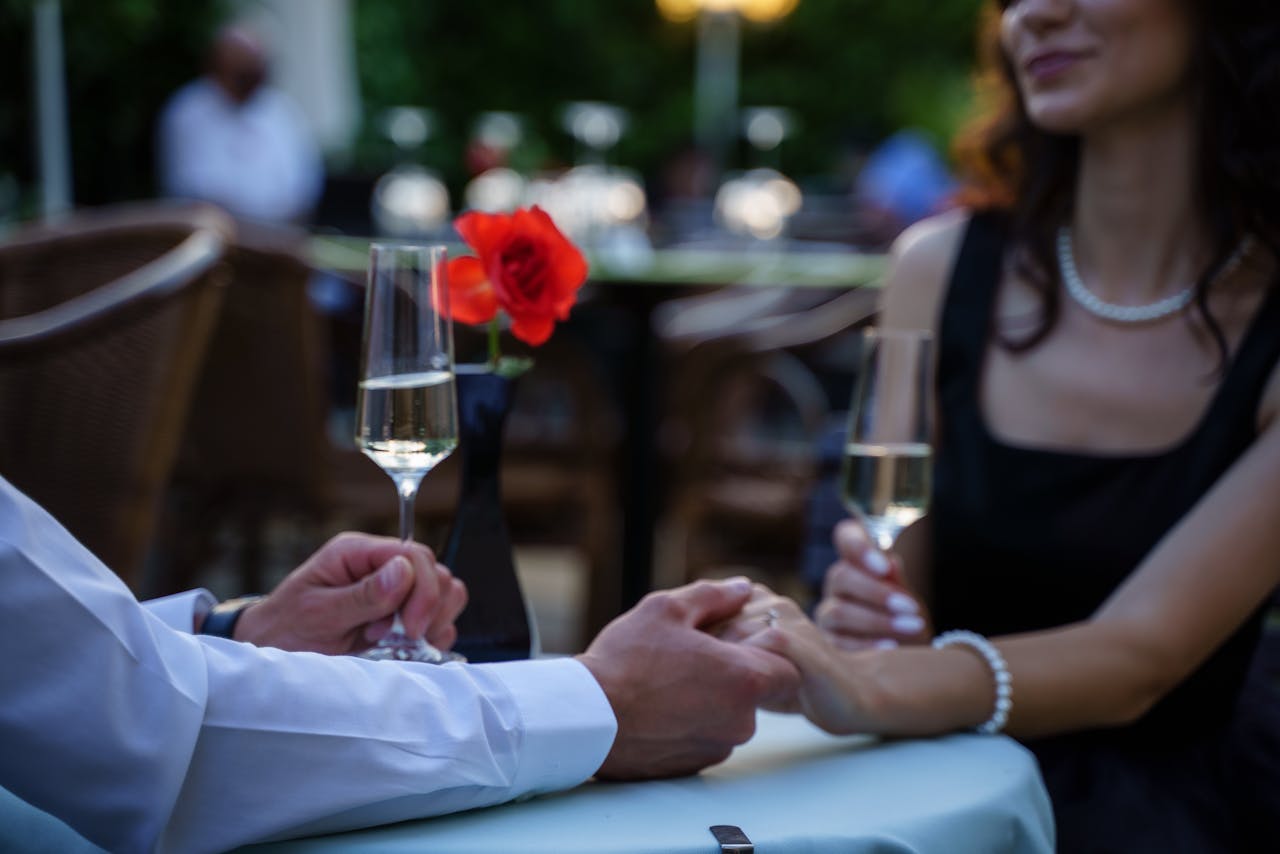 A romantic moment with a couple holding hands at a candlelit outdoor restaurant table.