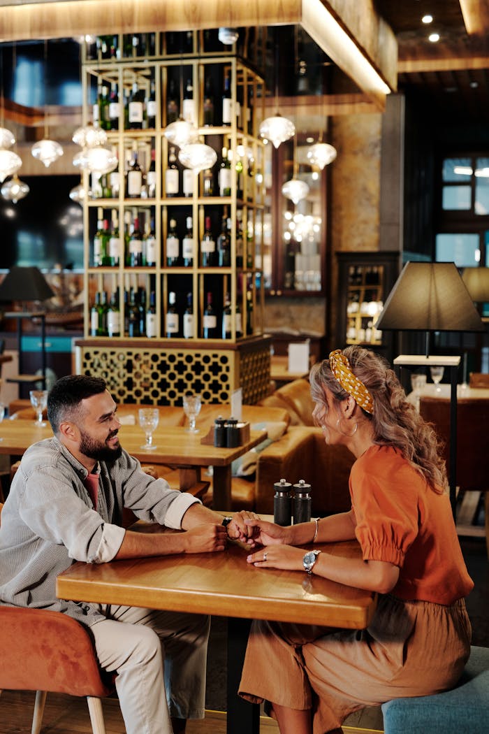 A couple holding hands and chatting during a date at a stylish restaurant interior.