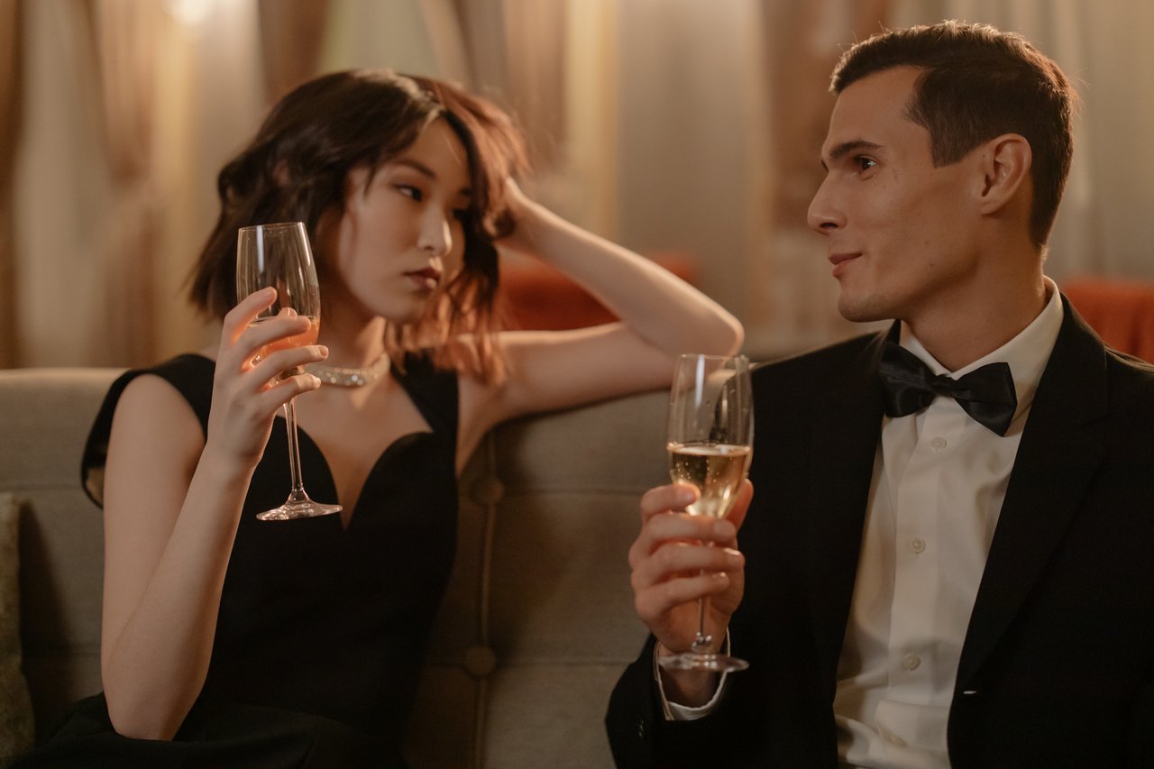 A stylish couple in formal attire enjoying champagne indoors, conveying elegance and romance.